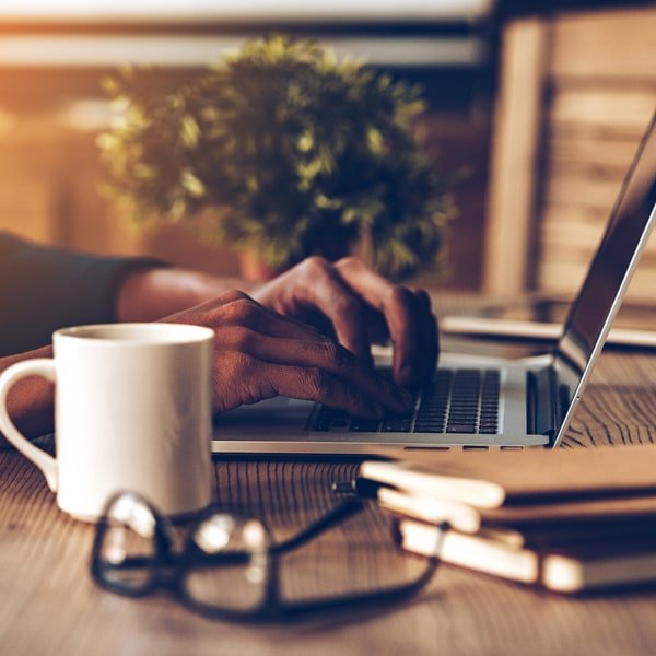 Person mit Kaffeebecher am Notebook